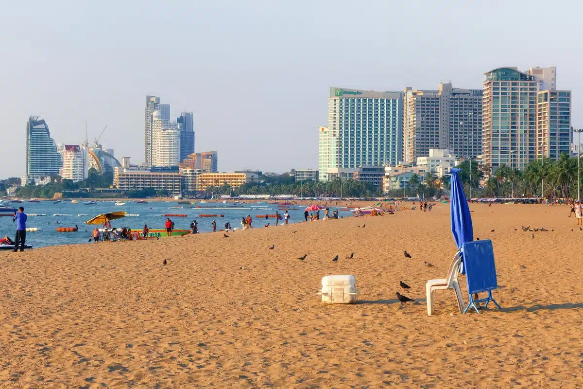 Beachfront in Pattaya with sunbathers, boats, and hotel skyline